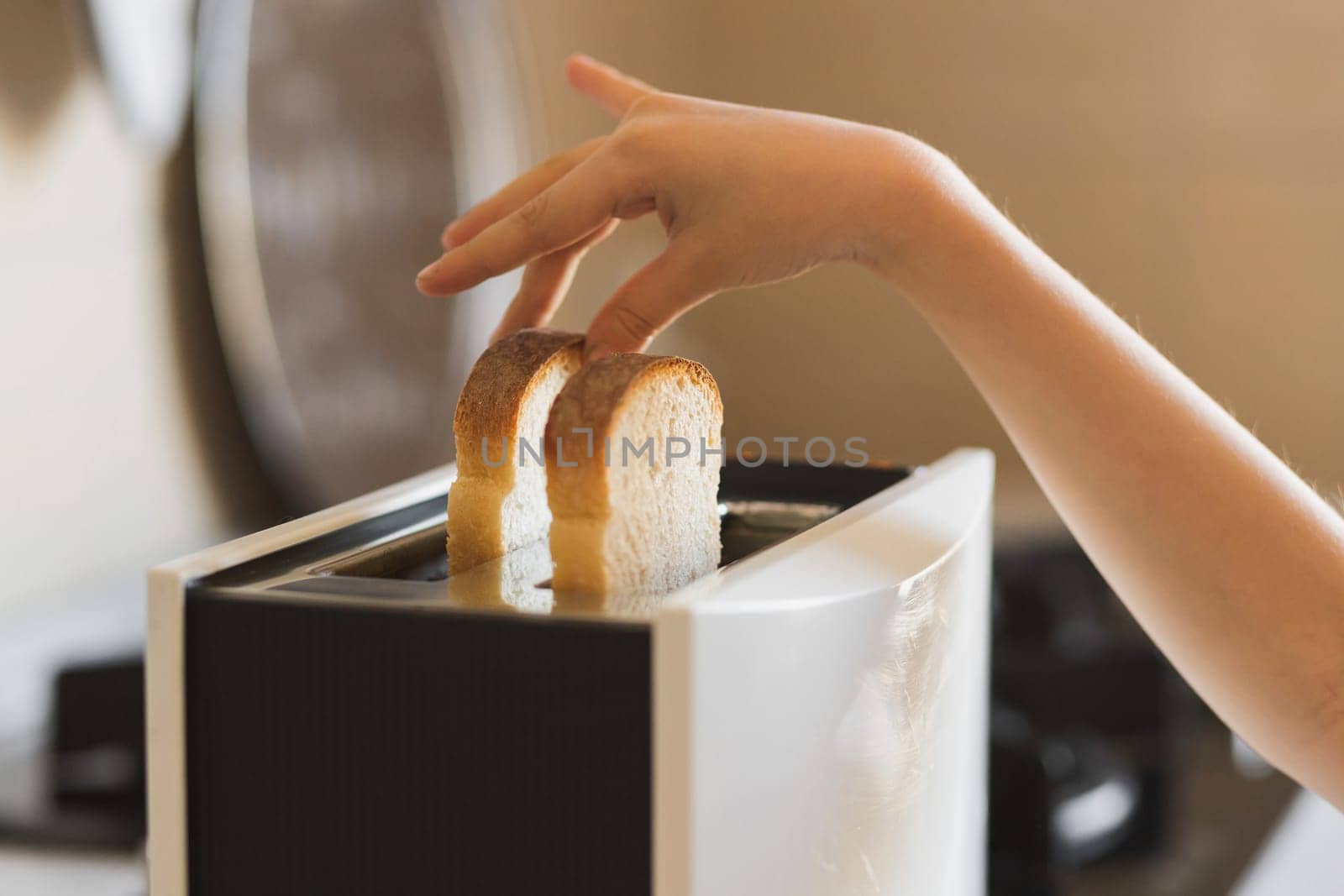 Close-up of a child's hand that inserts white slices of bread into a toaster.
