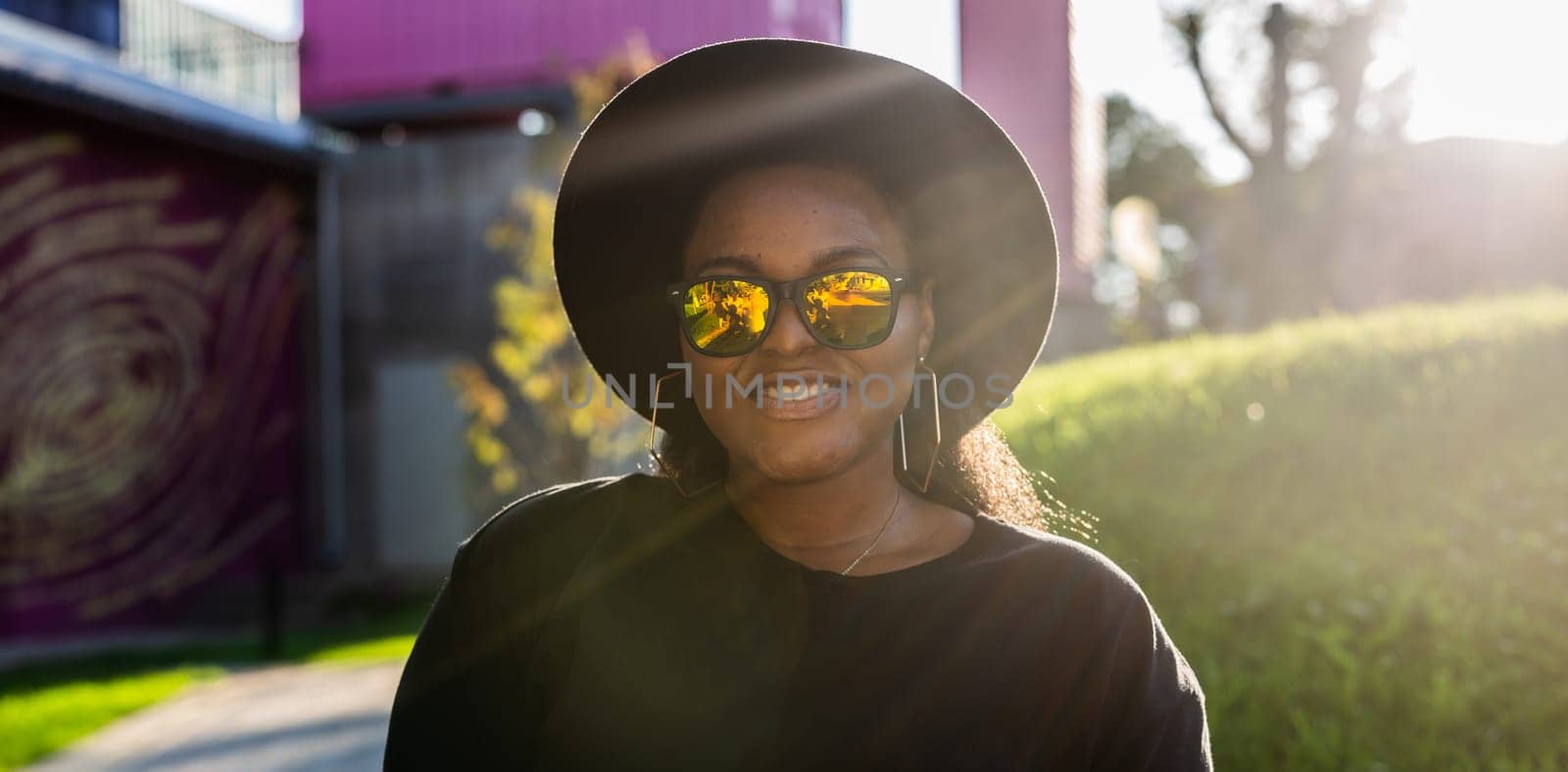 African american woman in an urban city area. Smiling generation z or millennial hipster girl posing outdoor backlit with sunlight portrait copy space by Satura86