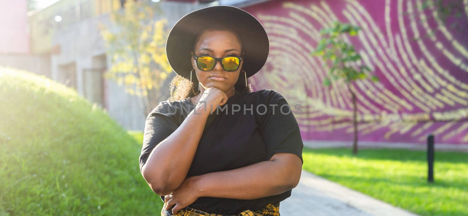 African american woman in an urban city area. Smiling generation z or millennial hipster girl posing outdoor backlit with sunlight portrait copy space by Satura86
