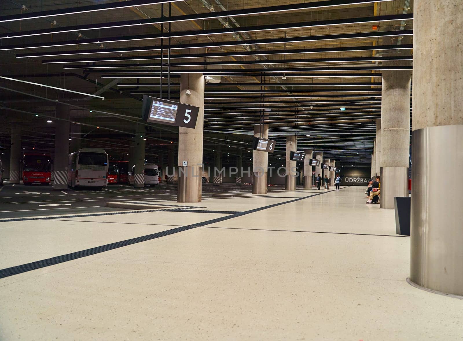 An empty bus station inside with parked buses and large columns by driver-s