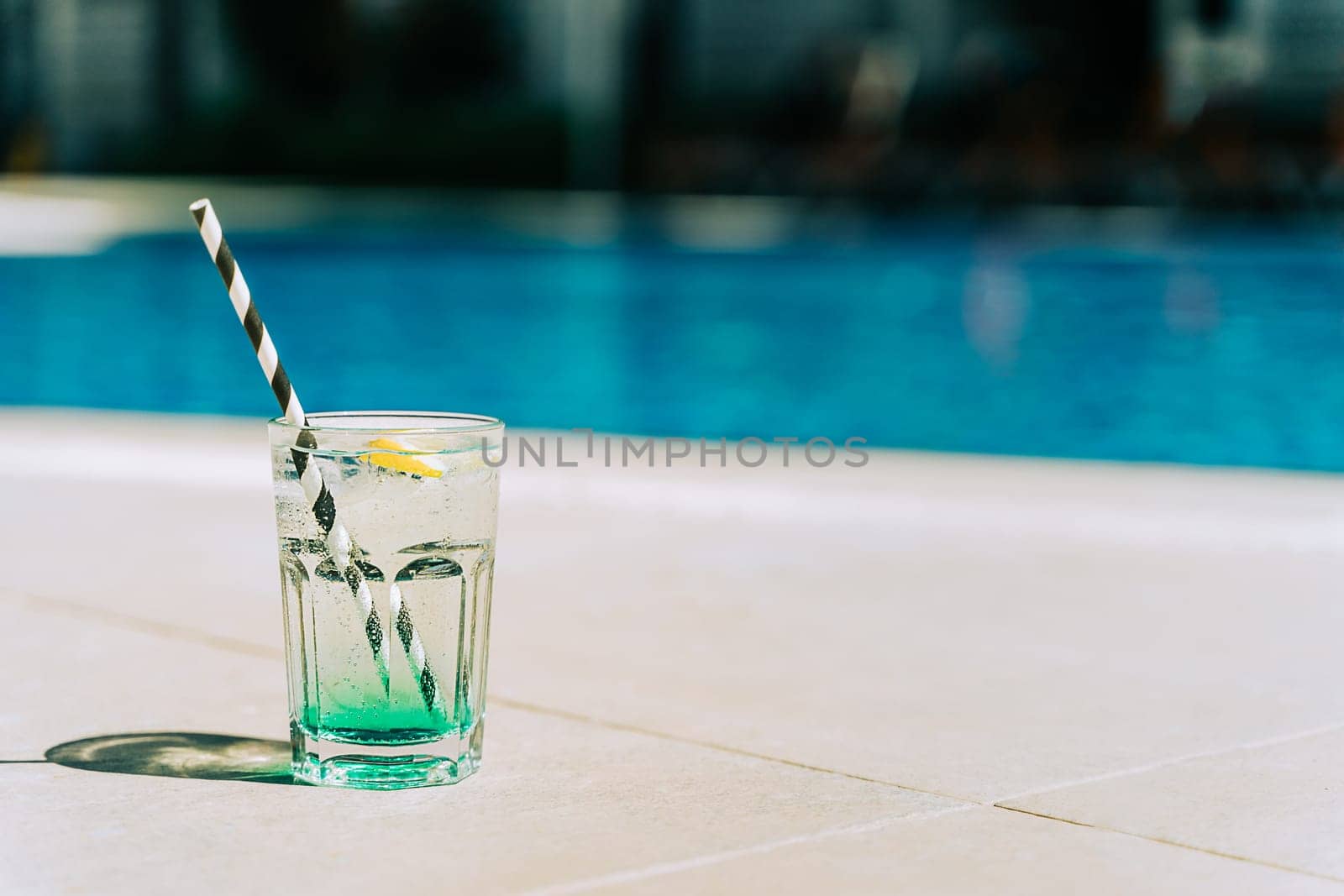 The glass of sparkling mint fruit cocktail standing by the swimming pool. Summer alcohol free drink by the hotel pool. Hello summer holiday vacation by Ostanina