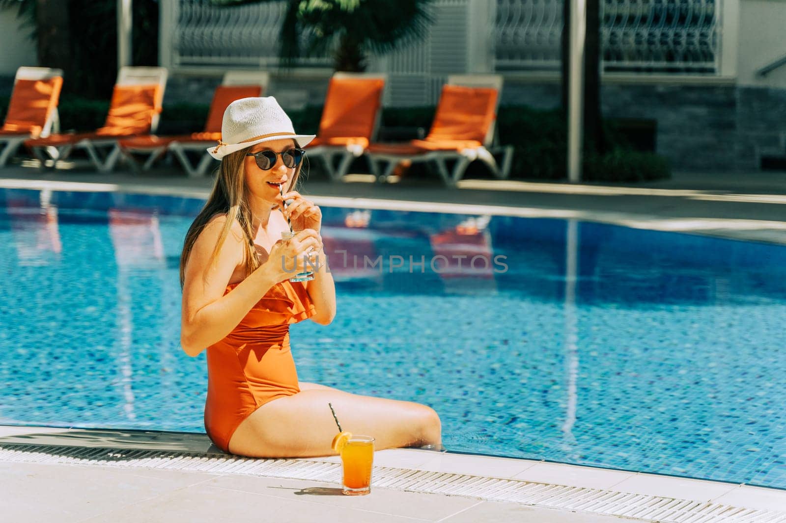 Beautiful young woman lady girl in a bikini, hat, and sunglasses enjoying cocktail lemonade while chilling by the swimming pool. Hello summer holiday vacation