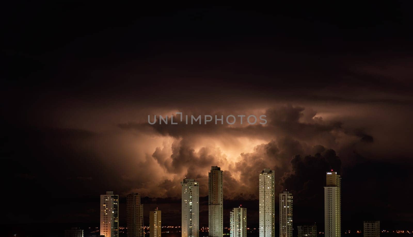 Dramatic orange storm clouds break through the night sky and hover over a city skyline of towering skyscrapers, creating a stunning contrast between light and dark. Copy space available.