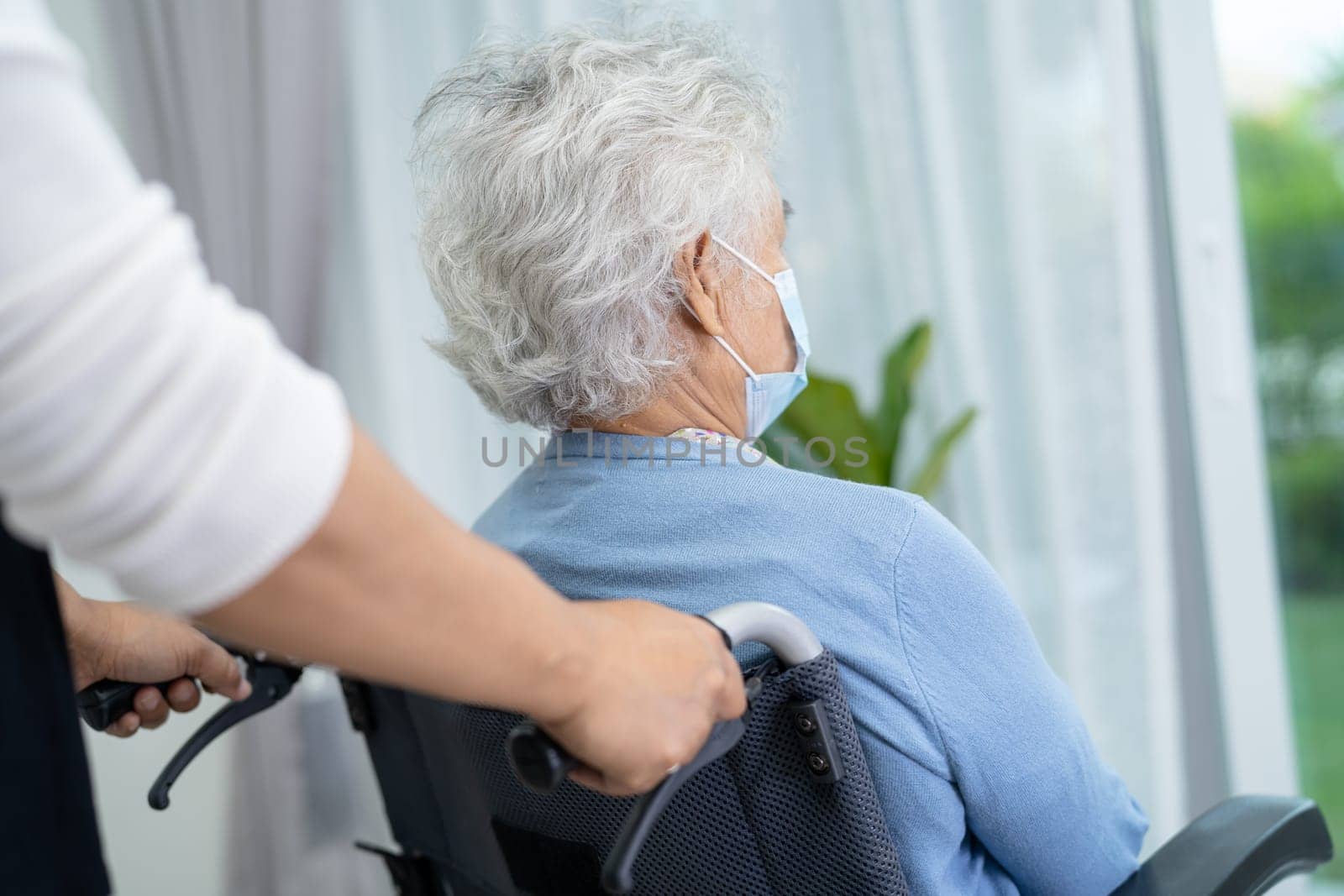 Caregiver help Asian senior woman on wheelchair and wearing a face mask for protect safety infection Covid19 Coronavirus. by pamai