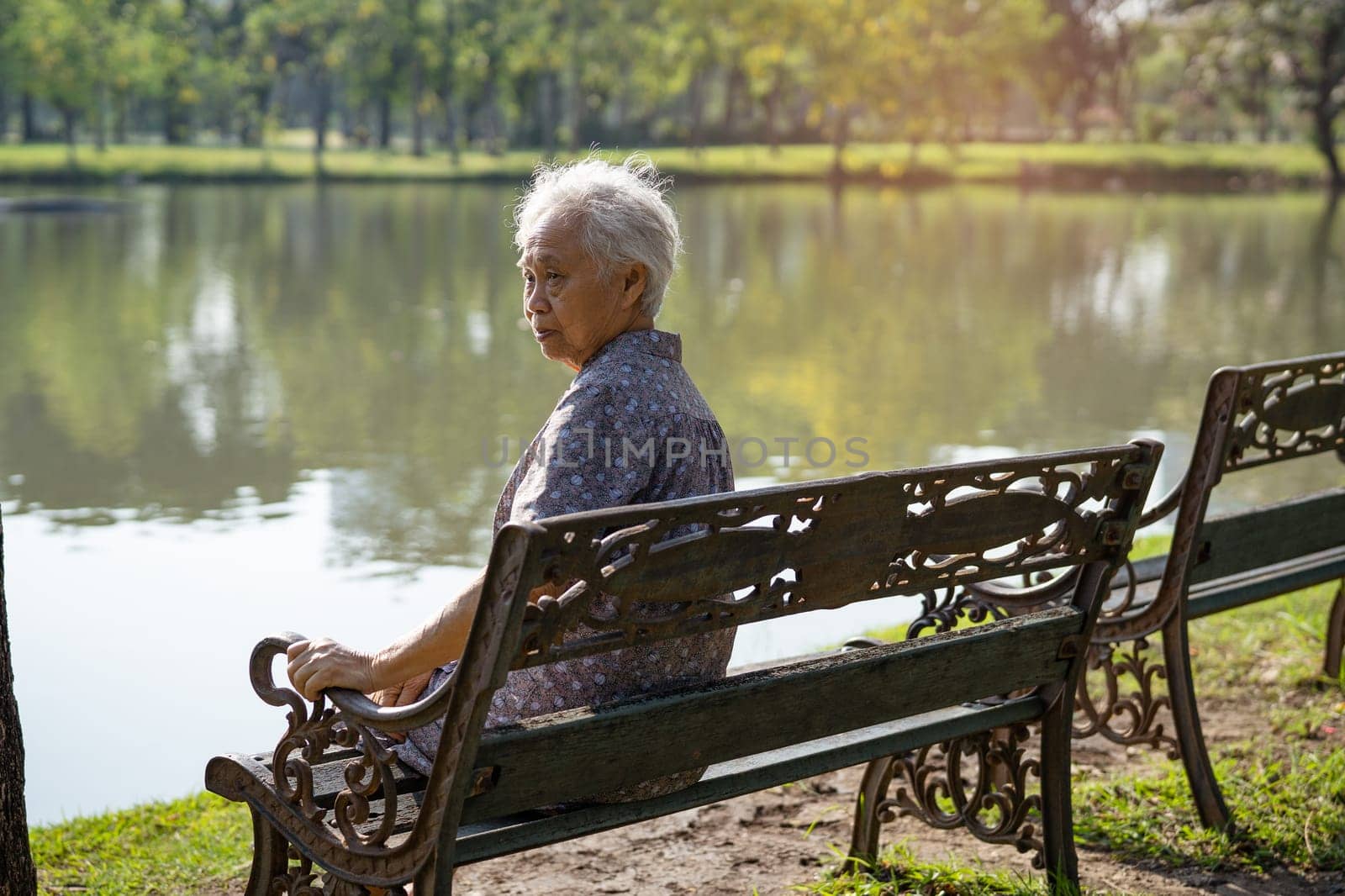 Asian elderly woman depressed and sad sitting back on bench in autumn park. by pamai