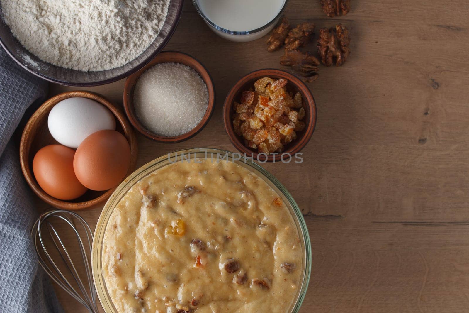 Preparation for cooking sweet pastries. Dough, eggs, sugar, milk, flour, salt, candied fruits, raisins, nuts, whisk on the kitchen table. copy space by lara29