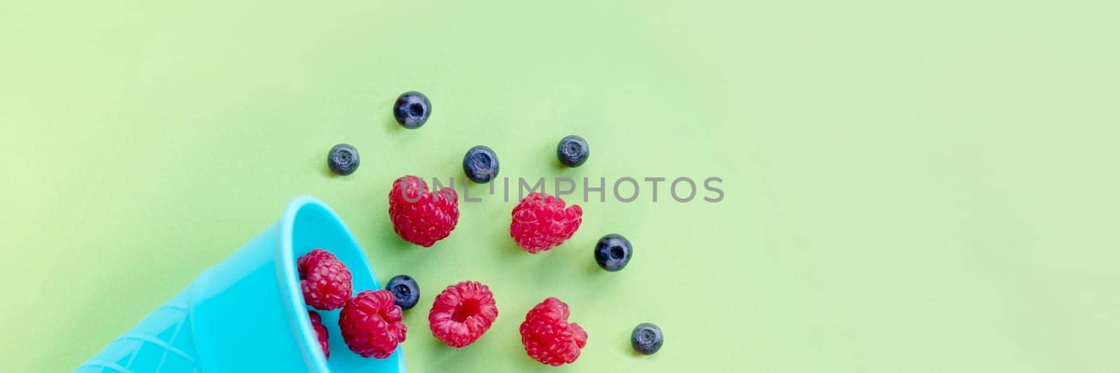 Waffle sweet ice cream cone with raspberries over white wooden background, top view.