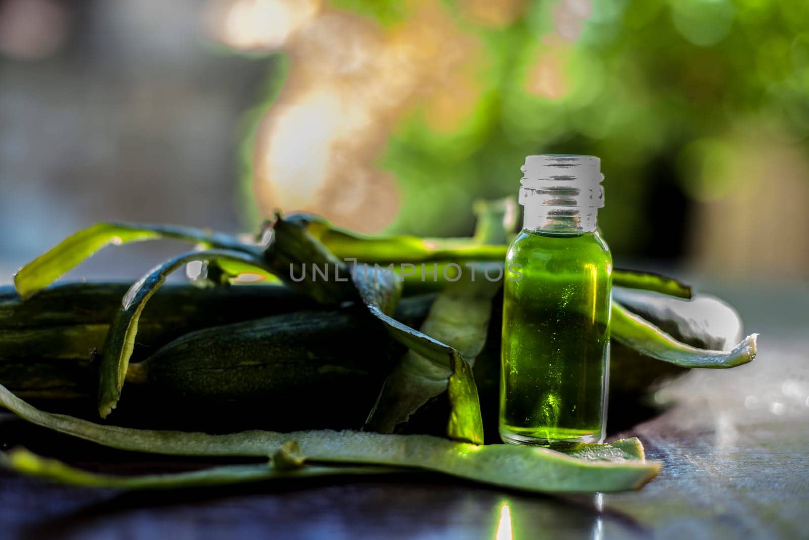 Close-up shot of fresh essential oil or sponge gourd or luffa in a glass bottle along with some fresh sponge gourd on the brown surface. by mirzamlk