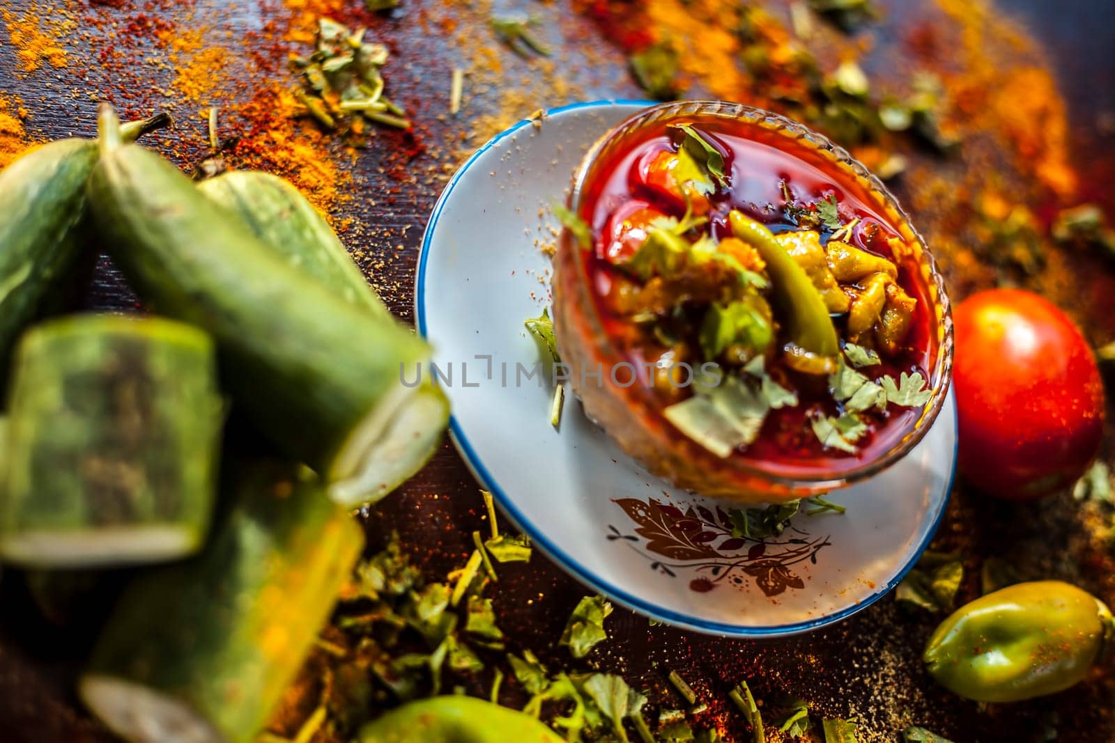 Close-up shot of fresh Indian Lunchtime dish luffa or Galka nu Shaak in a glass container along with all its ingredients on a rust-colored surface. by mirzamlk