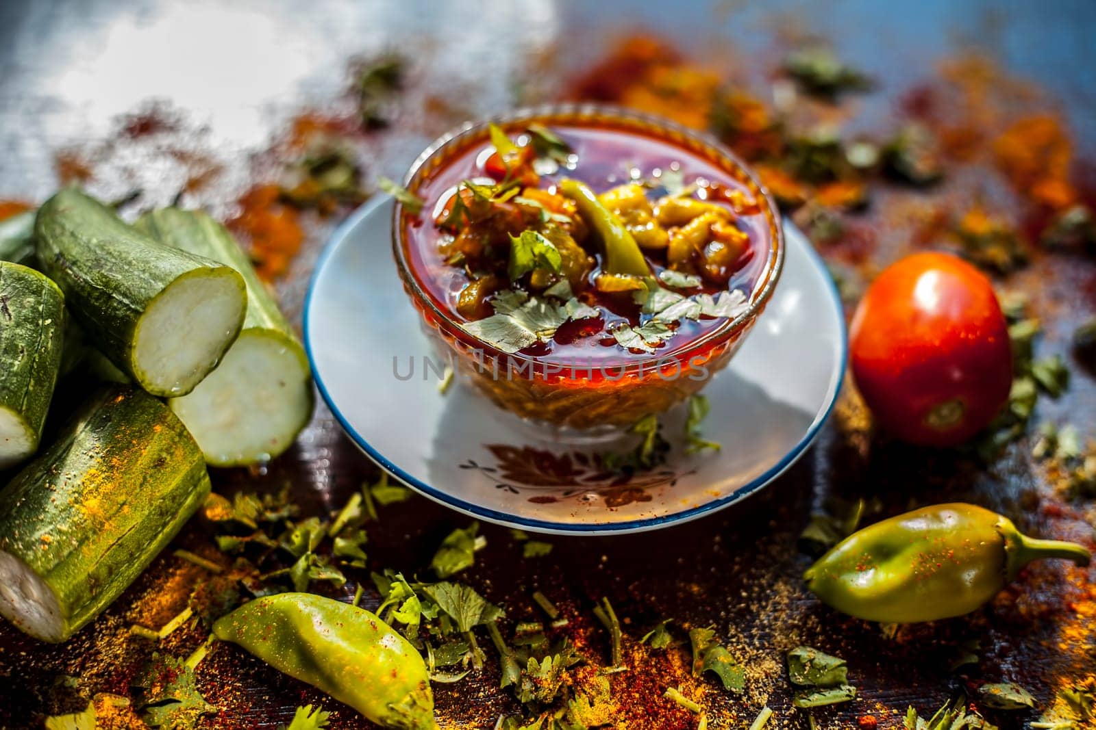 Close-up shot of fresh Indian Lunchtime dish luffa or Galka nu Shaak in a glass container along with all its ingredients on a rust-colored surface. by mirzamlk