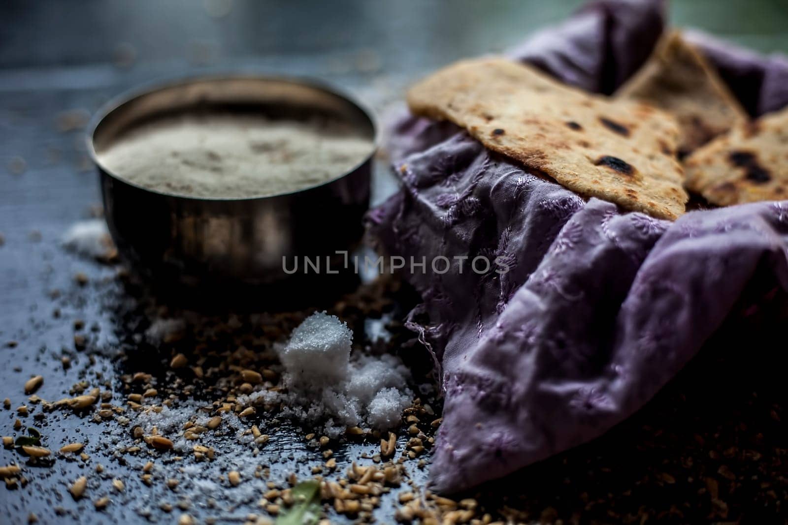 Shot of Gujarati breakfast consisting of round bread bhakri and lasun chutney. Shot of bhakhri, with wheat flour, garlic chutney, salt, ginger, and some whole wheat grains on a black glossy surface. by mirzamlk
