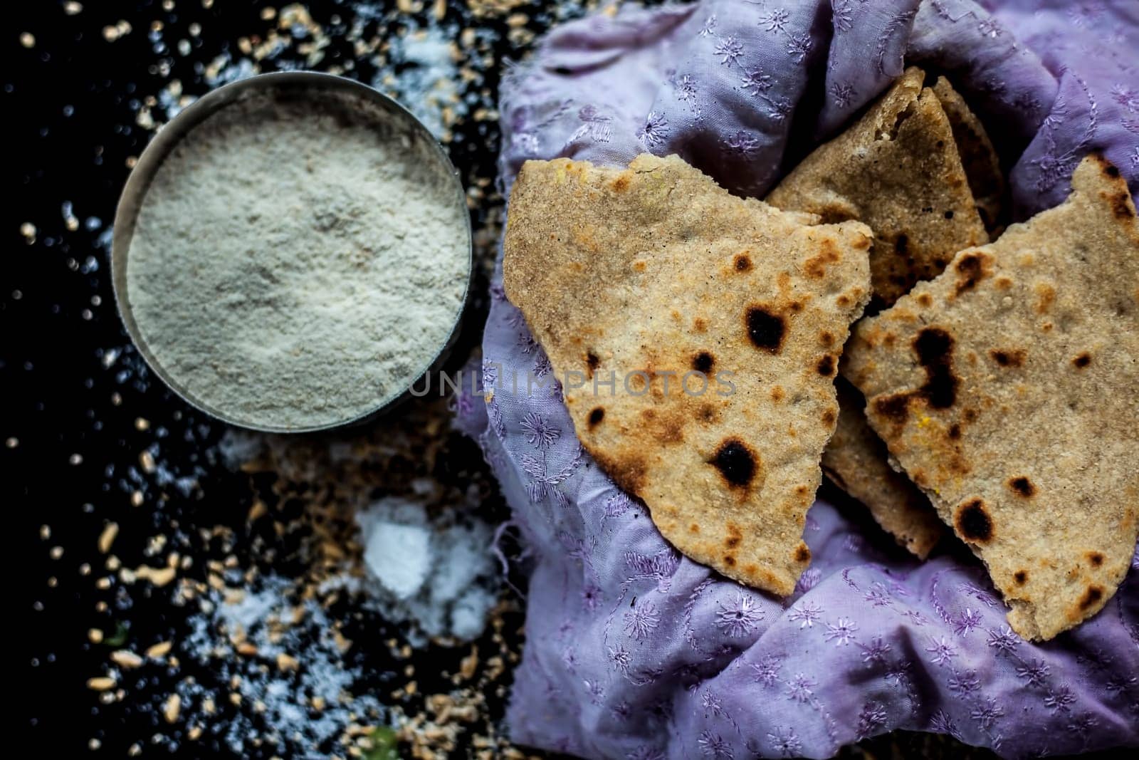 Shot of Gujarati breakfast consisting of round bread bhakri and lasun chutney. Shot of bhakhri, with wheat flour, garlic chutney, salt, ginger, and some whole wheat grains on a black glossy surface. by mirzamlk