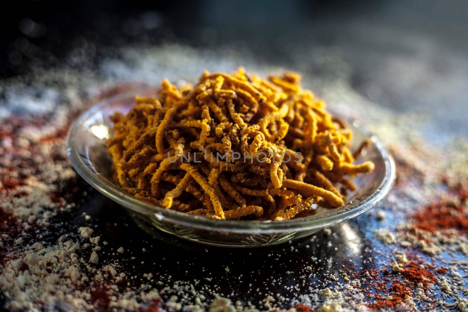 Diwali and Shravan Som special Teekha Gathiya in a glass plate along with some spread chickpea flour, red chili powder, and other ingredients that are needed to make the snack on a black surface. by mirzamlk