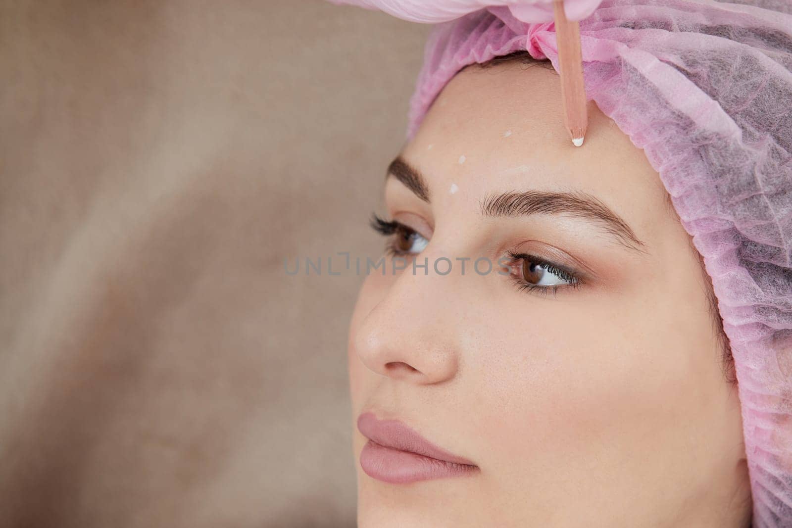 Cosmetologist drawing mark on client face to prepare for rejuvenation treatment