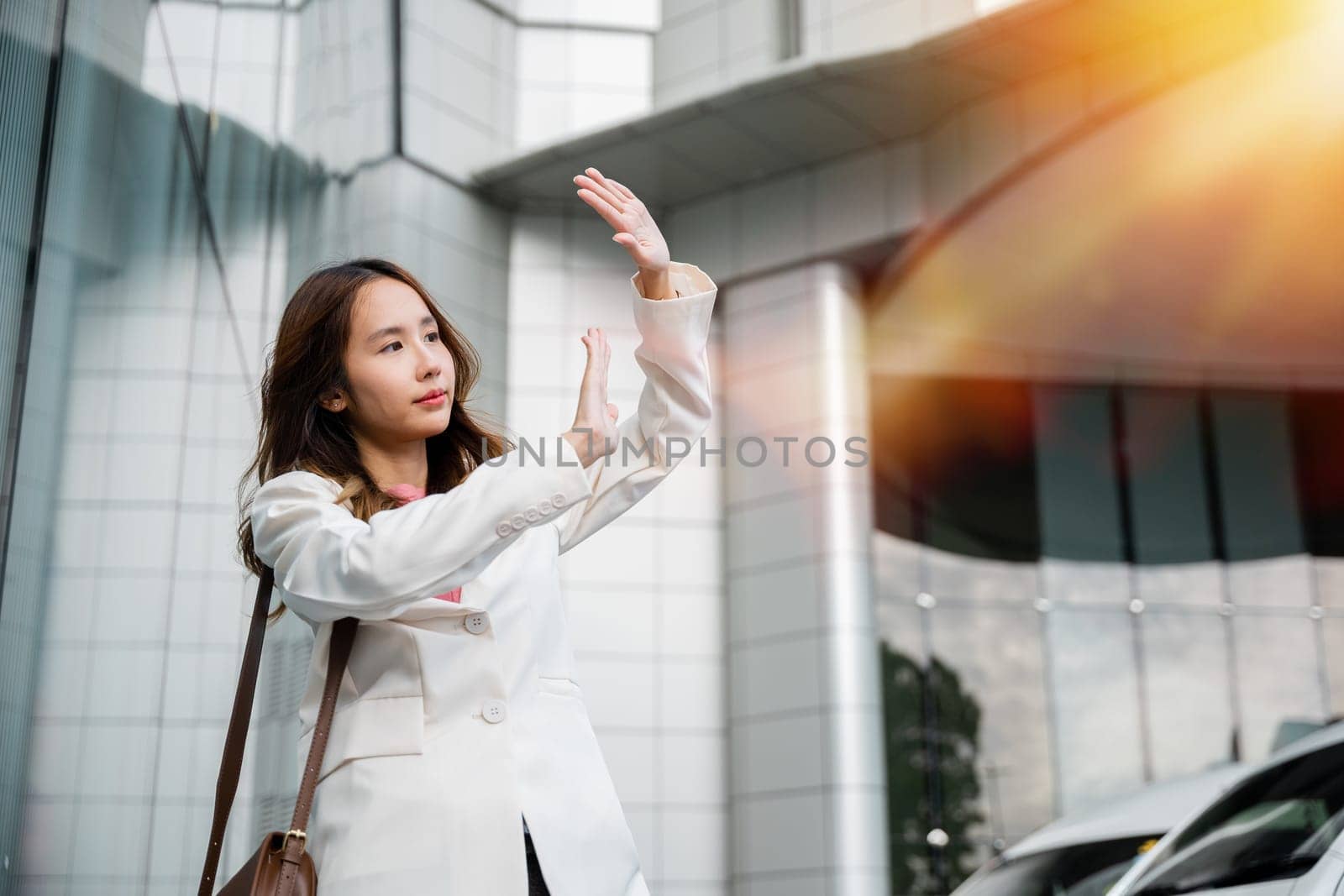 businesswoman standing outside office building in city raise your hand to shade the sun by Sorapop