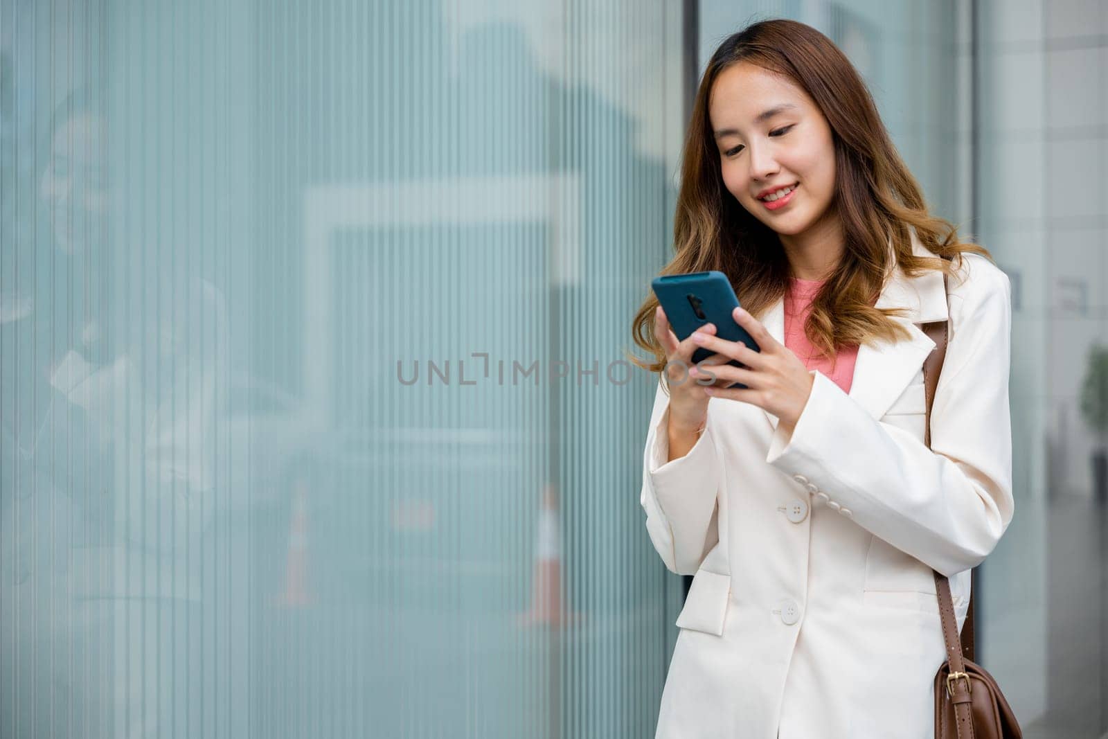 Asian businesswoman texting smartphone commuting work she walking near her office building in morning, Beautiful business woman smiling hold mobile phone outdoor walking on city street urban