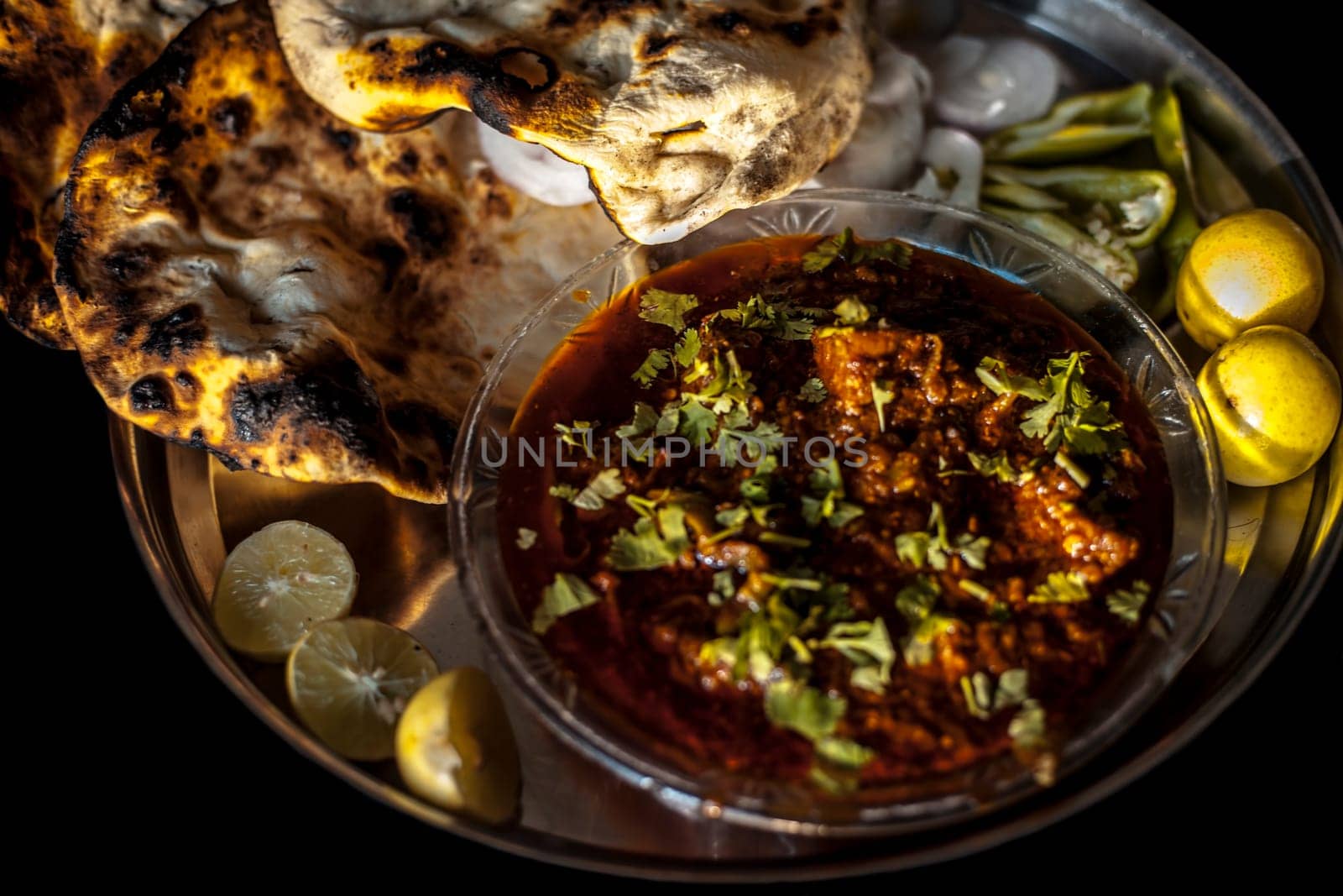 Shot of Achari Chicken along with tandoori roti with it on a serving plate with some chilies, onions, and lemons.