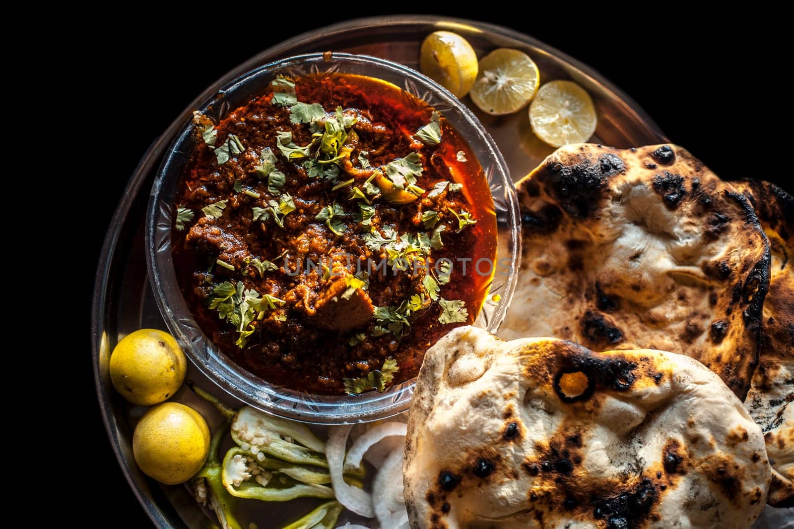 Shot of Achari Chicken along with tandoori roti with it on a serving plate with some chilies, onions, and lemons.