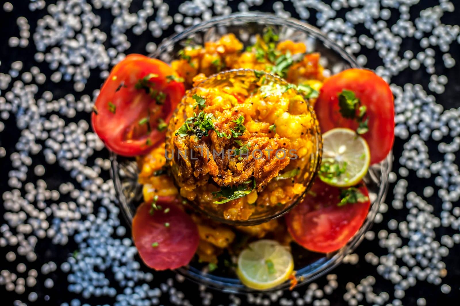Close-up shot of spicy tasty sabudana khichdi or sago ball khichdi along with some sliced tomatoes, some cut lemons in a glass plate, and raw sago balls.
