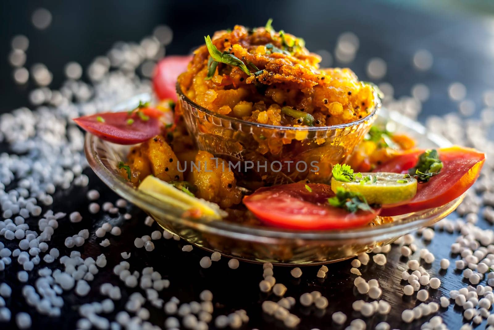 Close-up shot of spicy tasty sabudana khichdi or sago ball khichdi along with some sliced tomatoes, some cut lemons in a glass plate, and raw sago balls. by mirzamlk