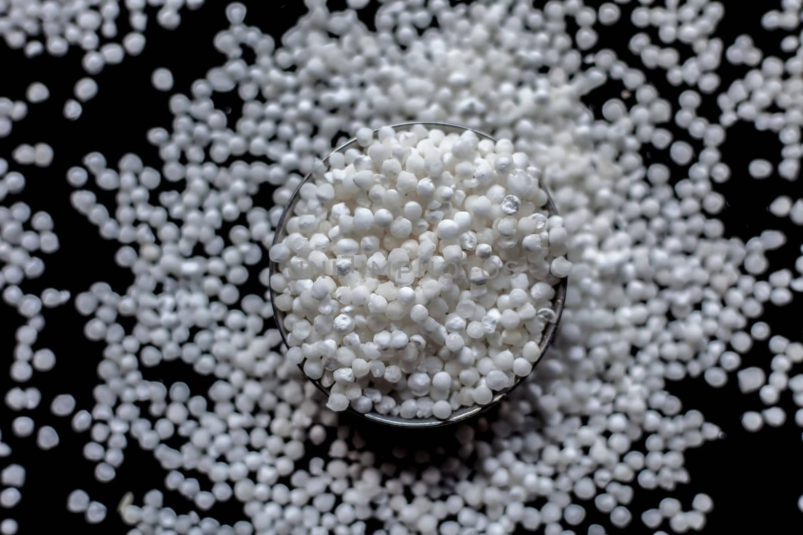 Close-up shot of raw sago pearls or tapioca pearls in a glass plate on a black-colored surface. by mirzamlk