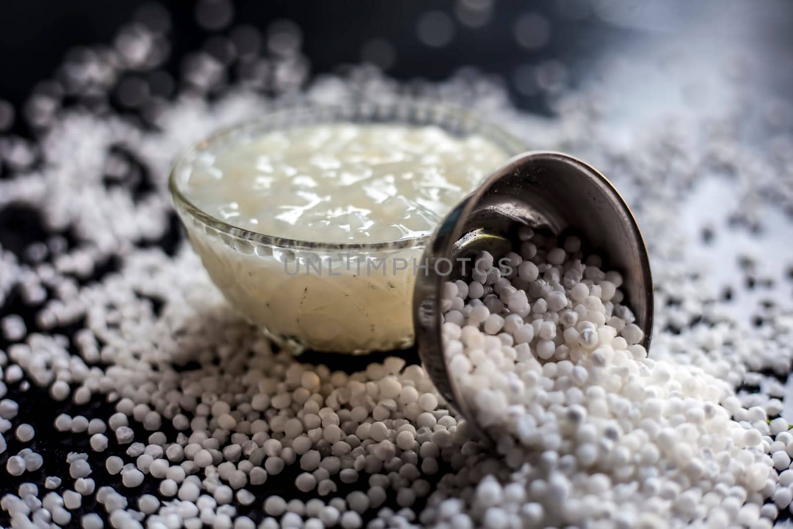 Close-up shot of sabudana ki kheer in a glass bowl along with some raw tapioca pearls and sugar spread on the surface.