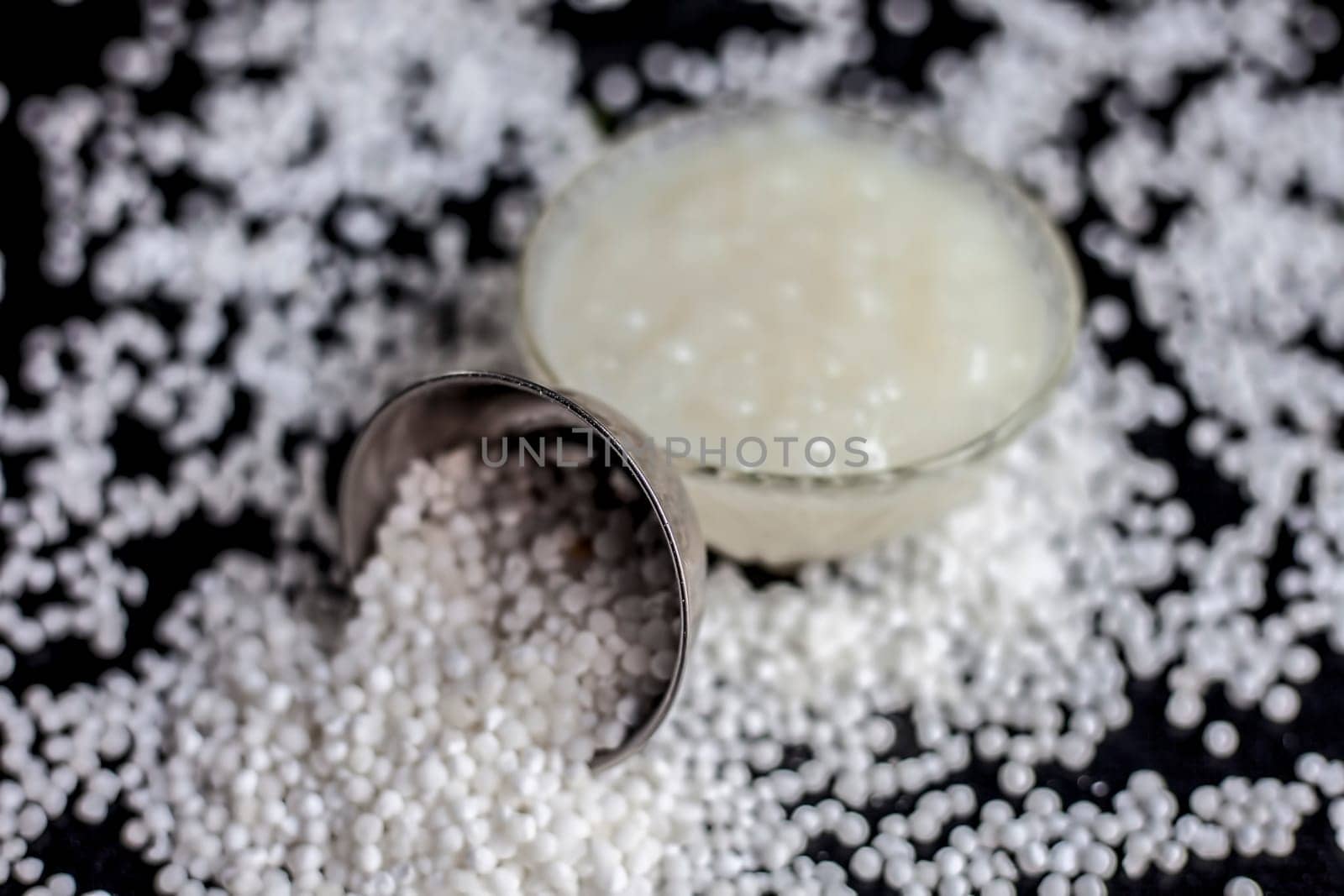 Close-up shot of sabudana ki kheer in a glass bowl along with some raw tapioca pearls and sugar spread on the surface.
