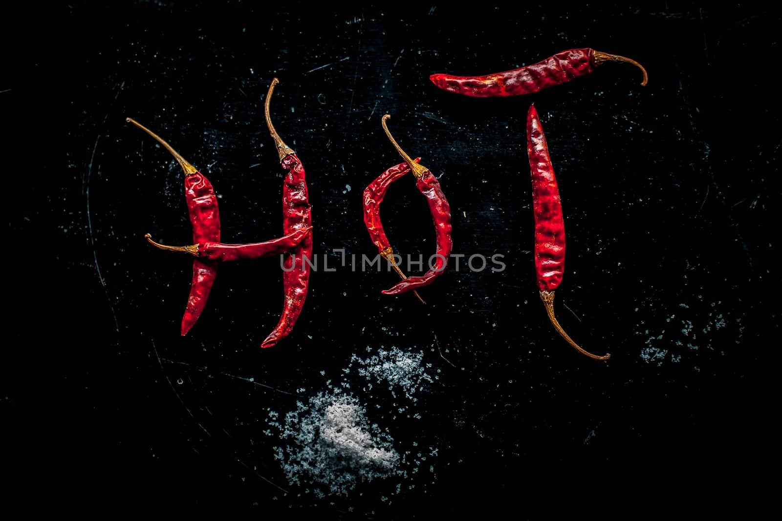HOT written on a black surface with the help of some red hot chilies. Top shot of red hot chilies making hot word. by mirzamlk