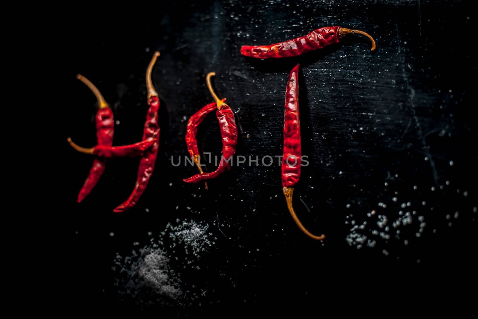 HOT written on a black surface with the help of some red hot chilies. Top shot of red hot chilies making hot word.