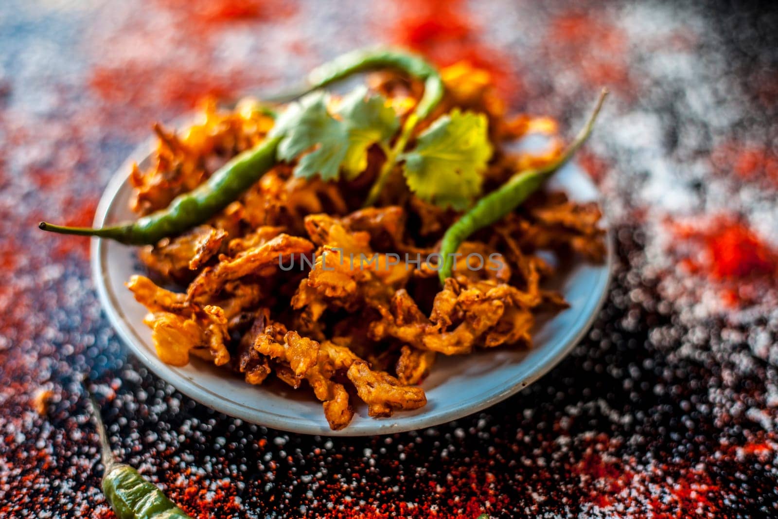 Shot of Indian tomato fritter on a glass plate along with some species on a black table. Shot of tomato pakora or tomato pakoda on a glass plate. by mirzamlk