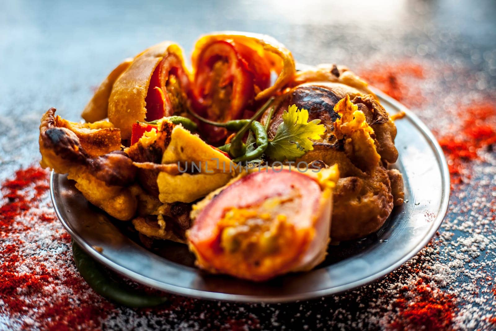 Shot of Indian tomato fritter on a glass plate along with some species on a black table. Shot of tomato pakora or tomato pakoda on a glass plate. by mirzamlk