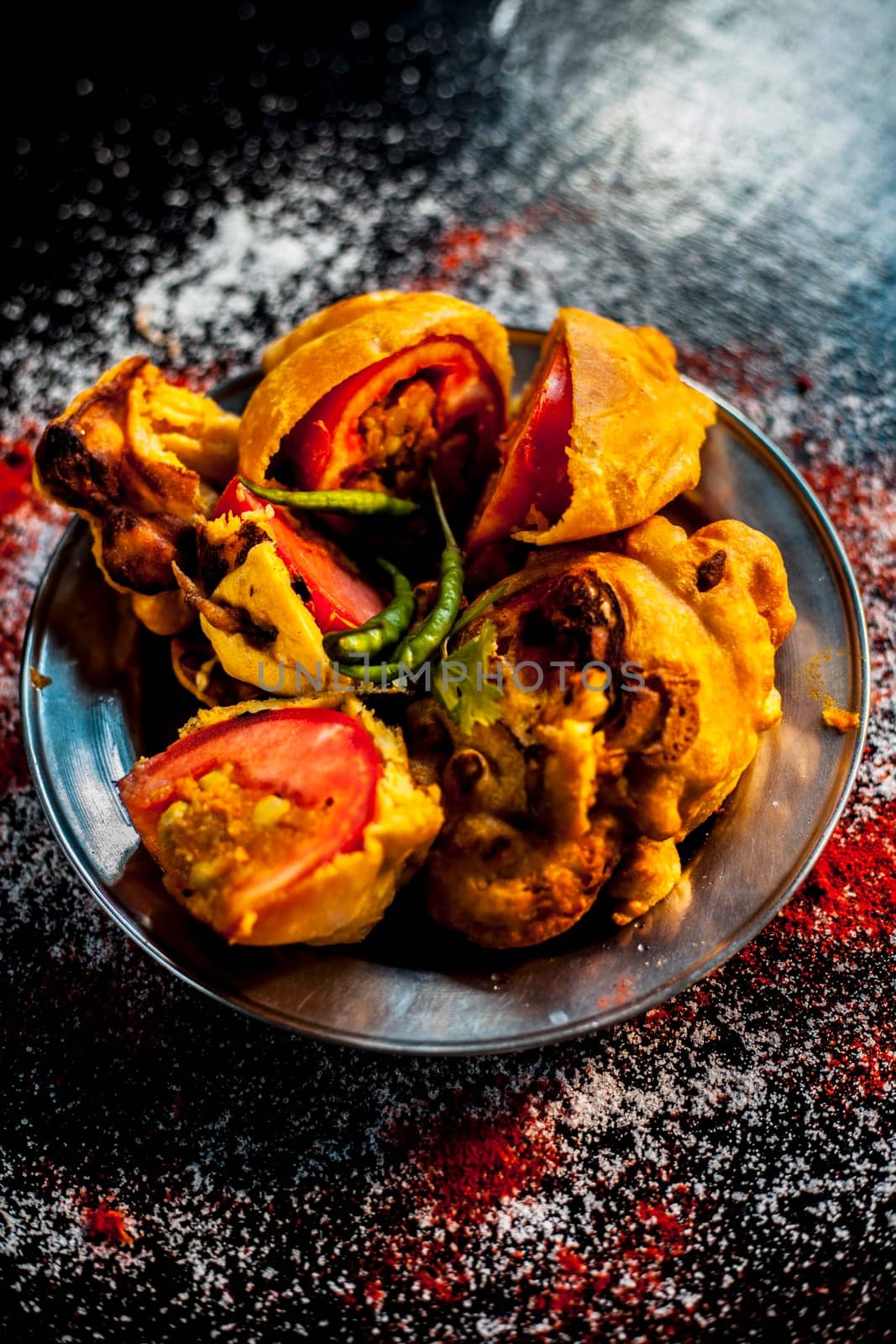 Shot of Indian tomato fritter on a glass plate along with some species on a black table. Shot of tomato pakora or tomato pakoda on a glass plate. by mirzamlk