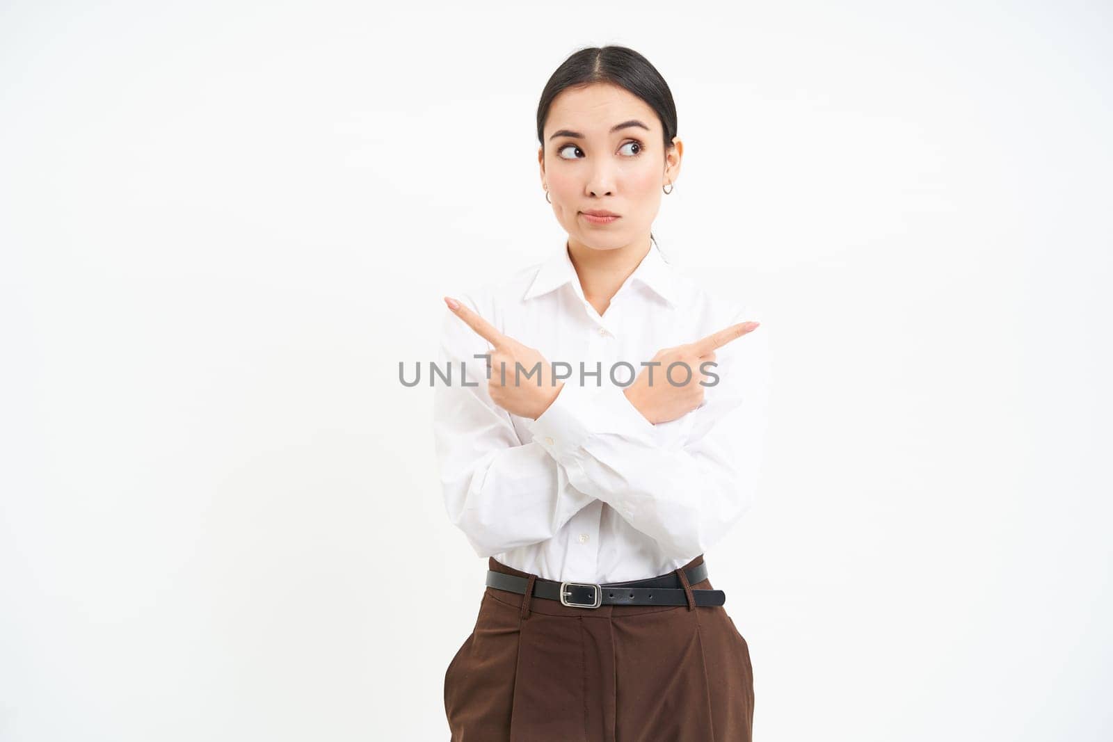 Puzzled businesswoman points sideways, shows two choices, makes decision, stands over white background.