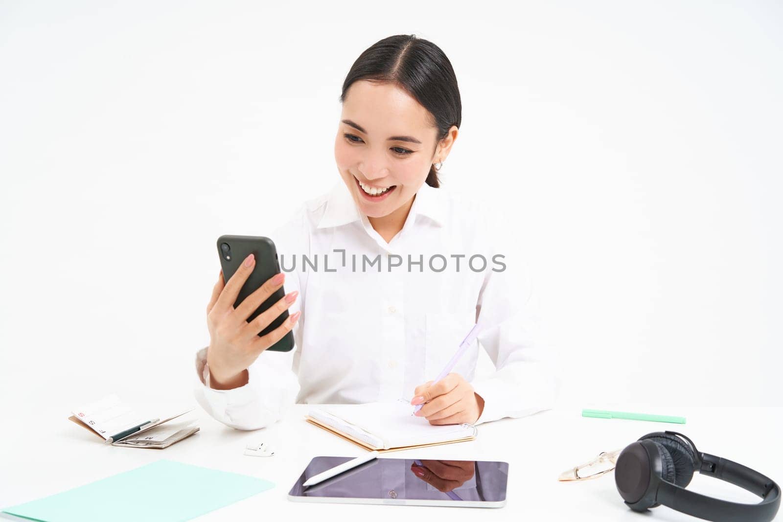 Young woman professional, businesswoman has a meeting on video chat, talks to mobile phone with client, stands over white background.