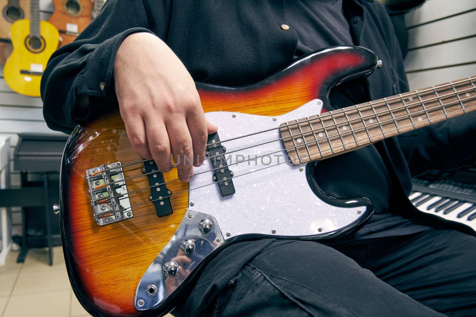 Demonstration of a bass guitar in a music store. Close-up of a man's hand playing the bass guitar