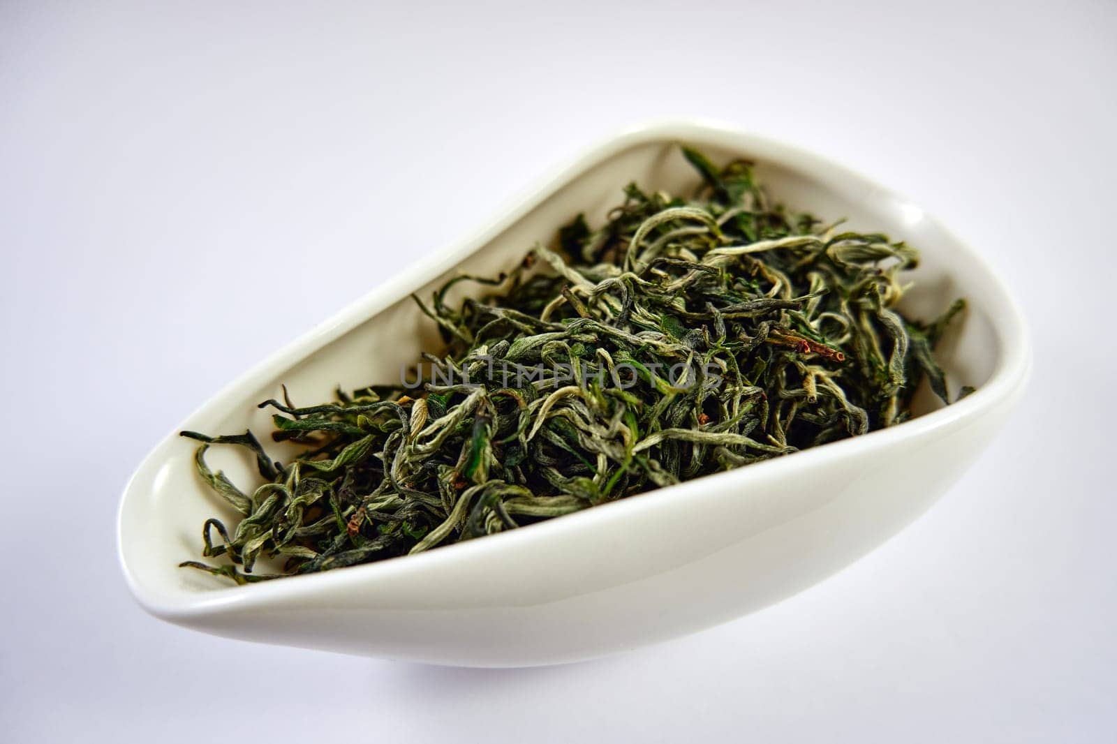 Dry Chinese green tea in a white porcelain bowl. Selective Focus