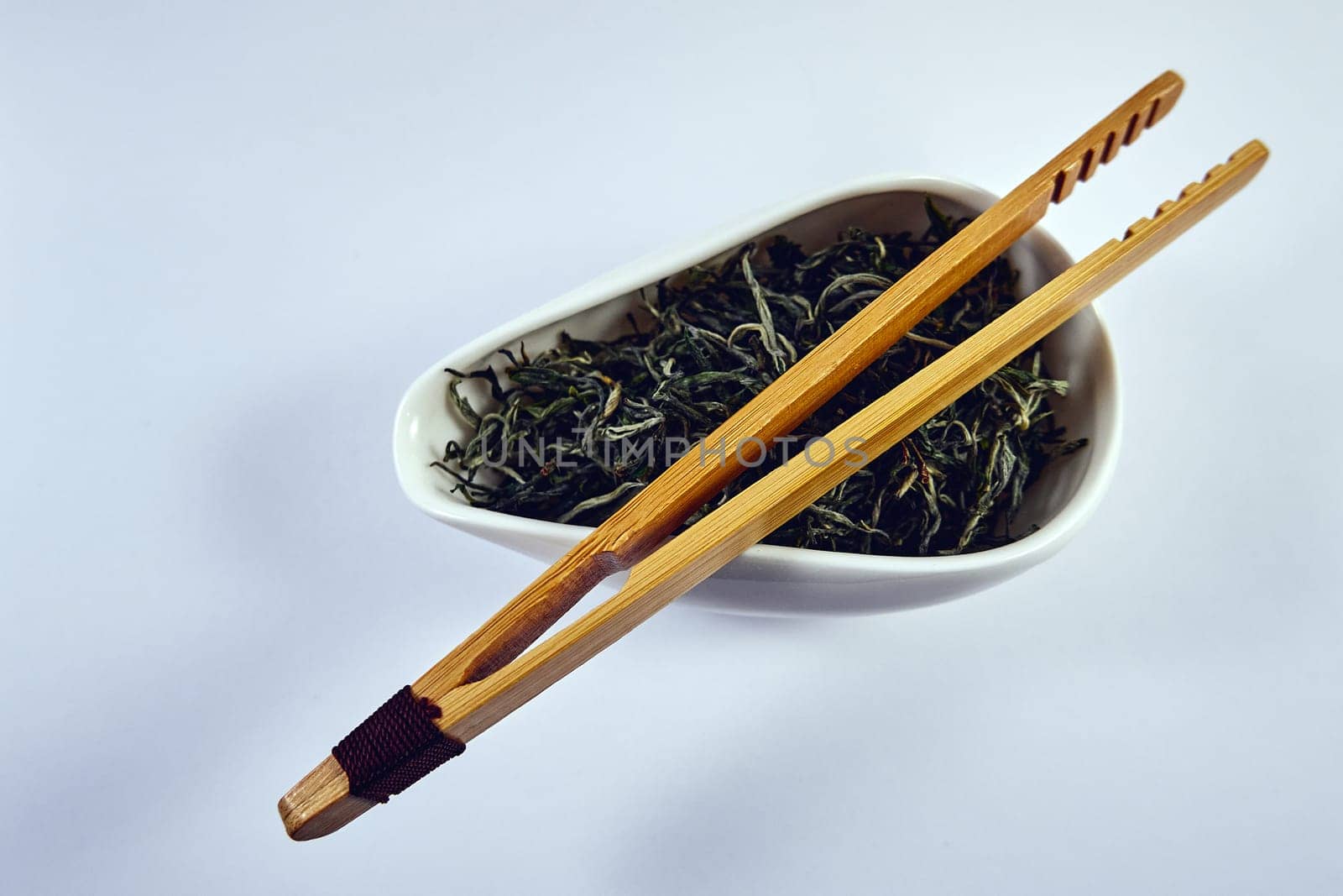 Dry green tea in a porcelain bowl and bamboo tongs. Tea ceremony