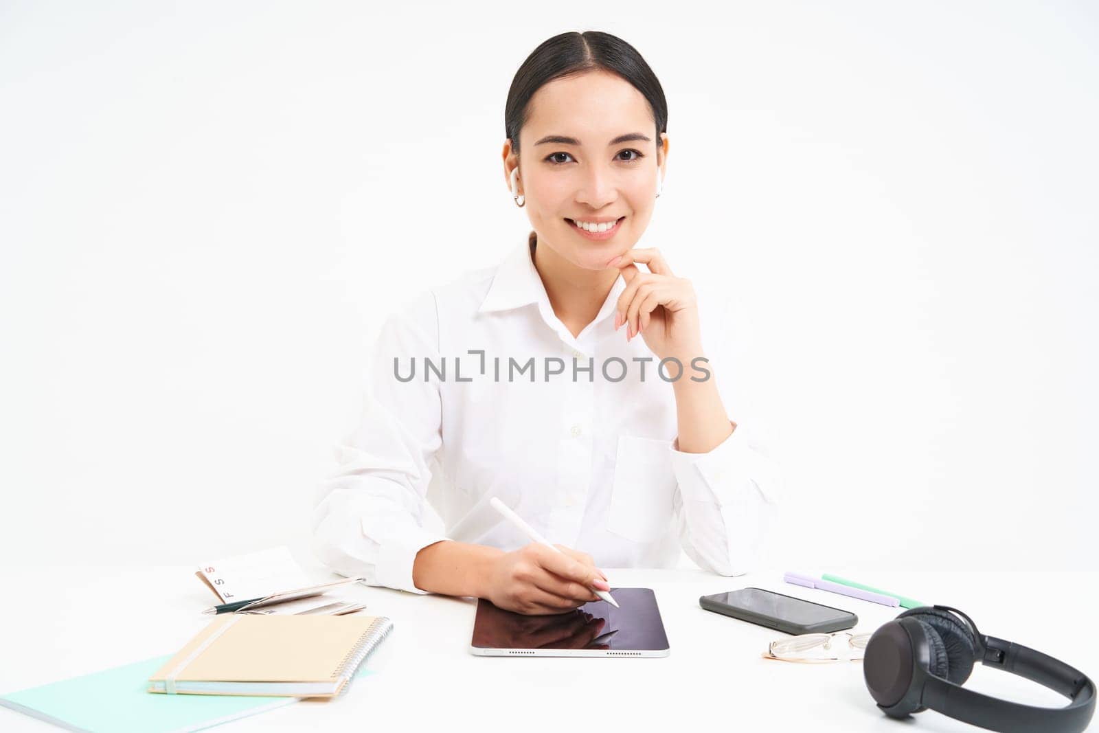 Young businesswoman sits in her office and writes on digital tablet, working in her company, isolated on white background.