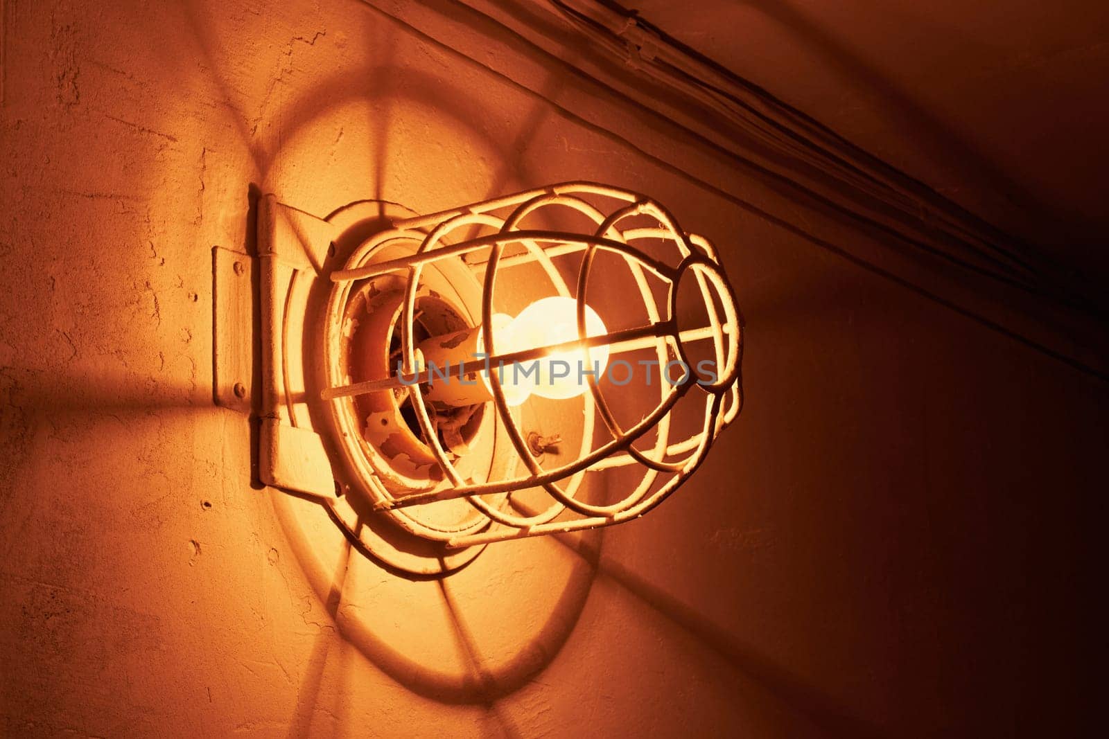 Luminous incandescent lamp. Old electric light bulb with a metal grate on the wall