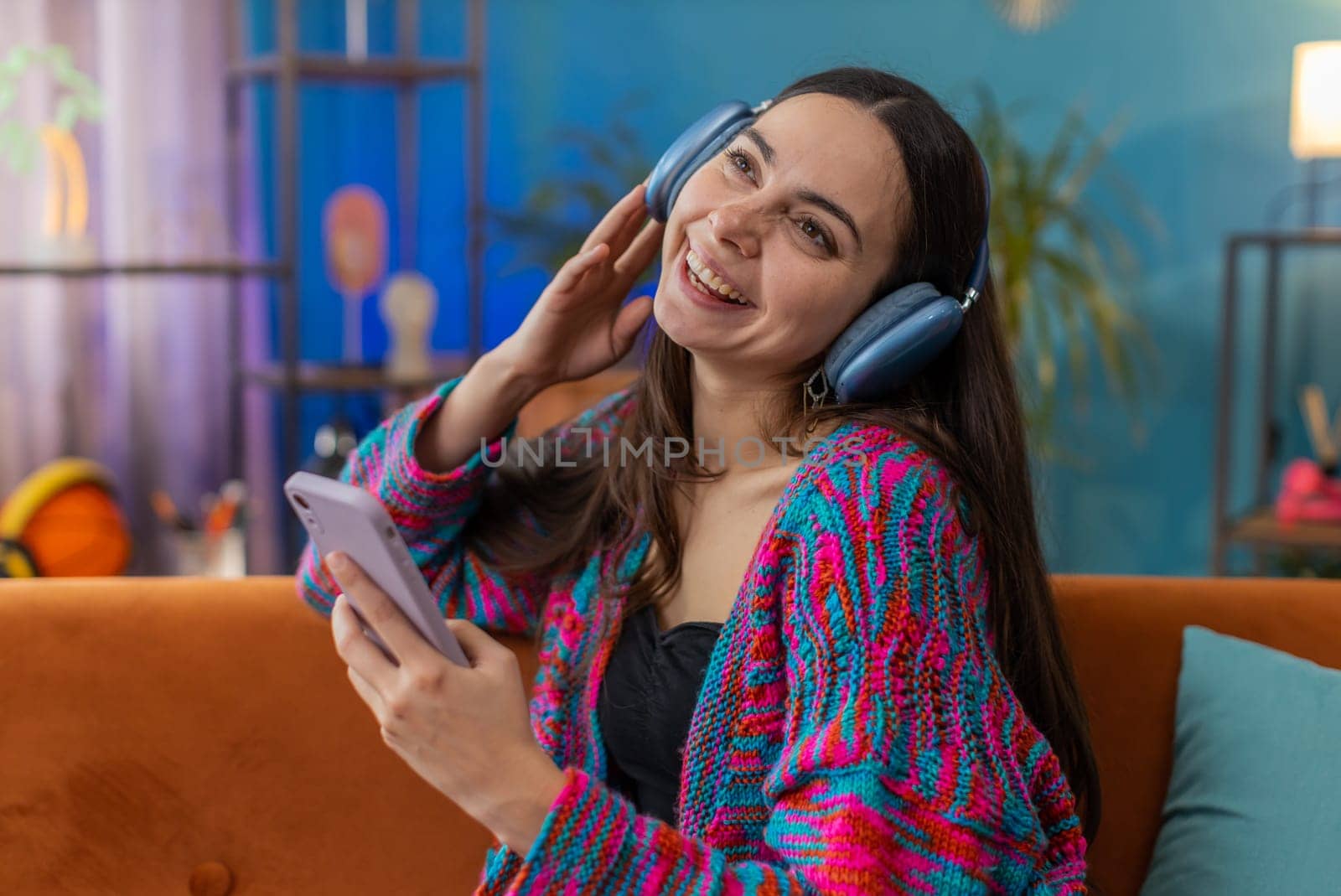 Happy overjoyed Caucasian woman in wireless headphones relaxing sitting on couch at home apartment choosing listening favorite energetic disco dancing music. People weekend daytime leisure activities