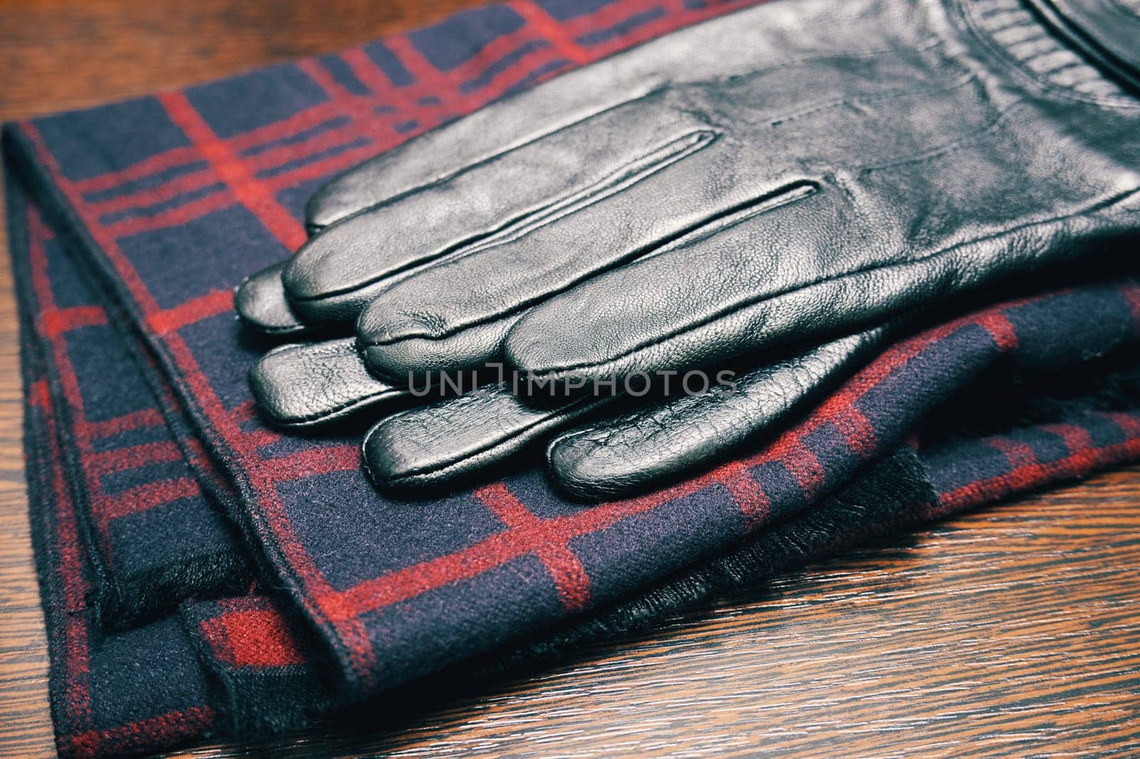 Men's leather gloves and a plaid scarf on a wooden table close-up