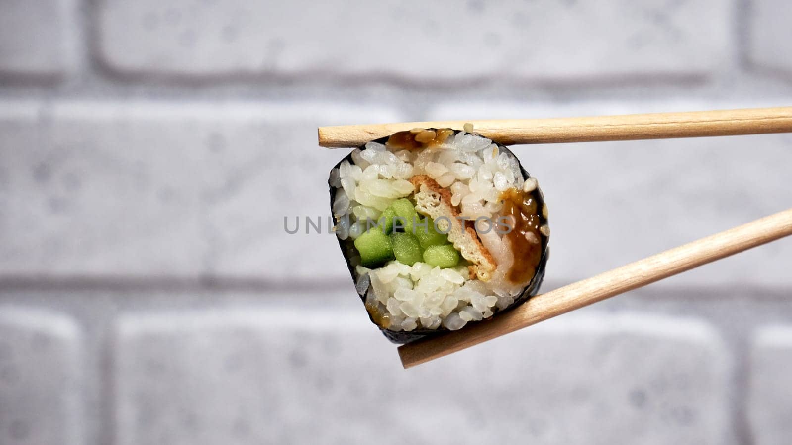Two chopsticks picking up a piece of sushi close up