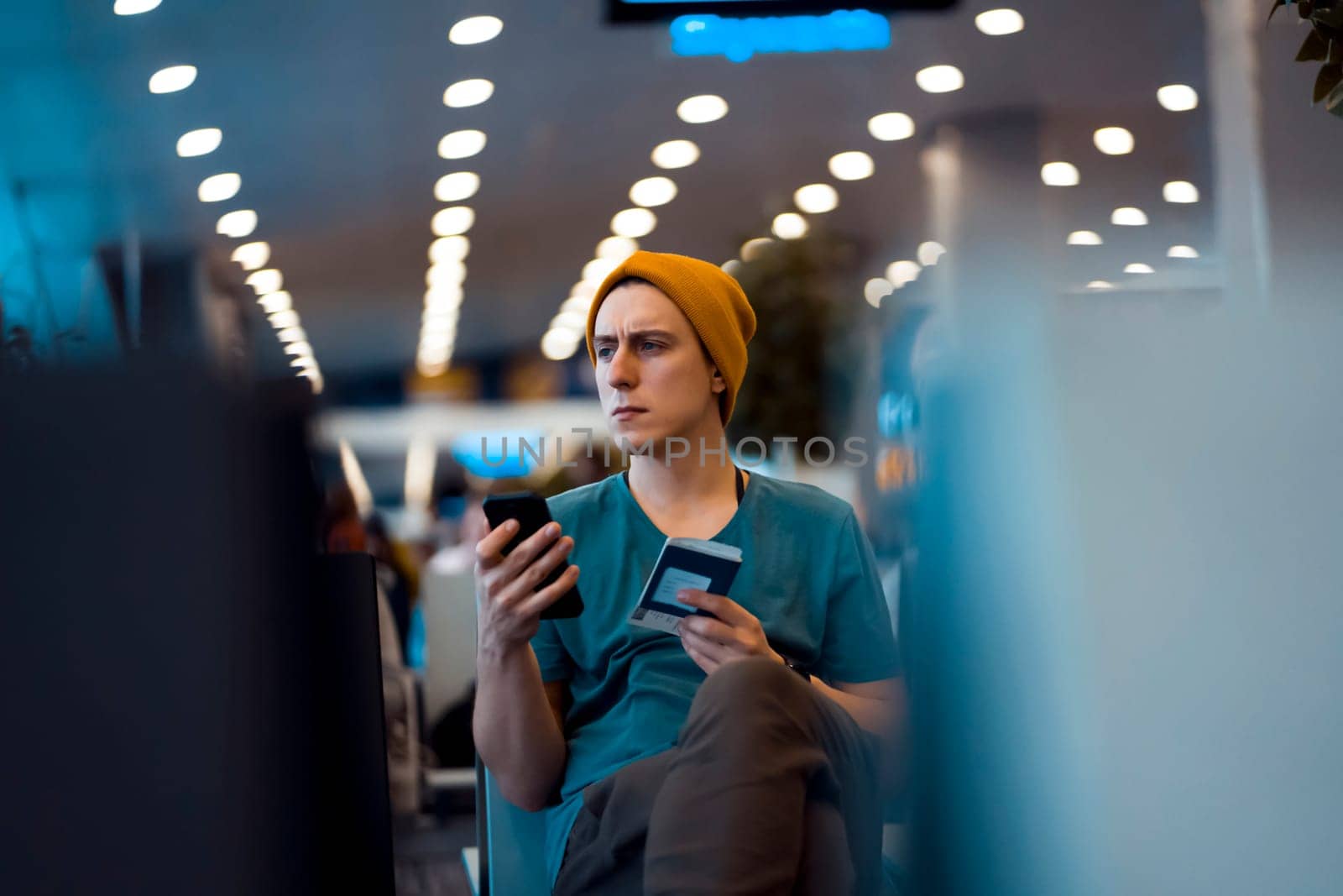 A young man sits at the airport and checks in for the next flight via an app on his phone, waits for the plane and works while traveling.