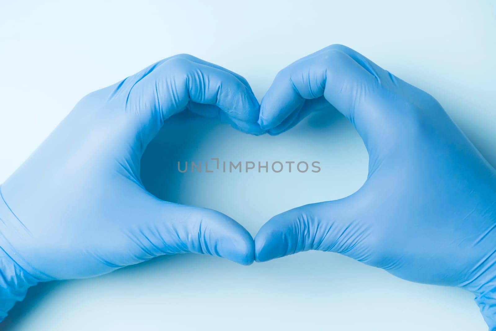 The hands of a doctor in blue gloves show the heart on a light background, as a symbol of medicine taking care of the patient's health.