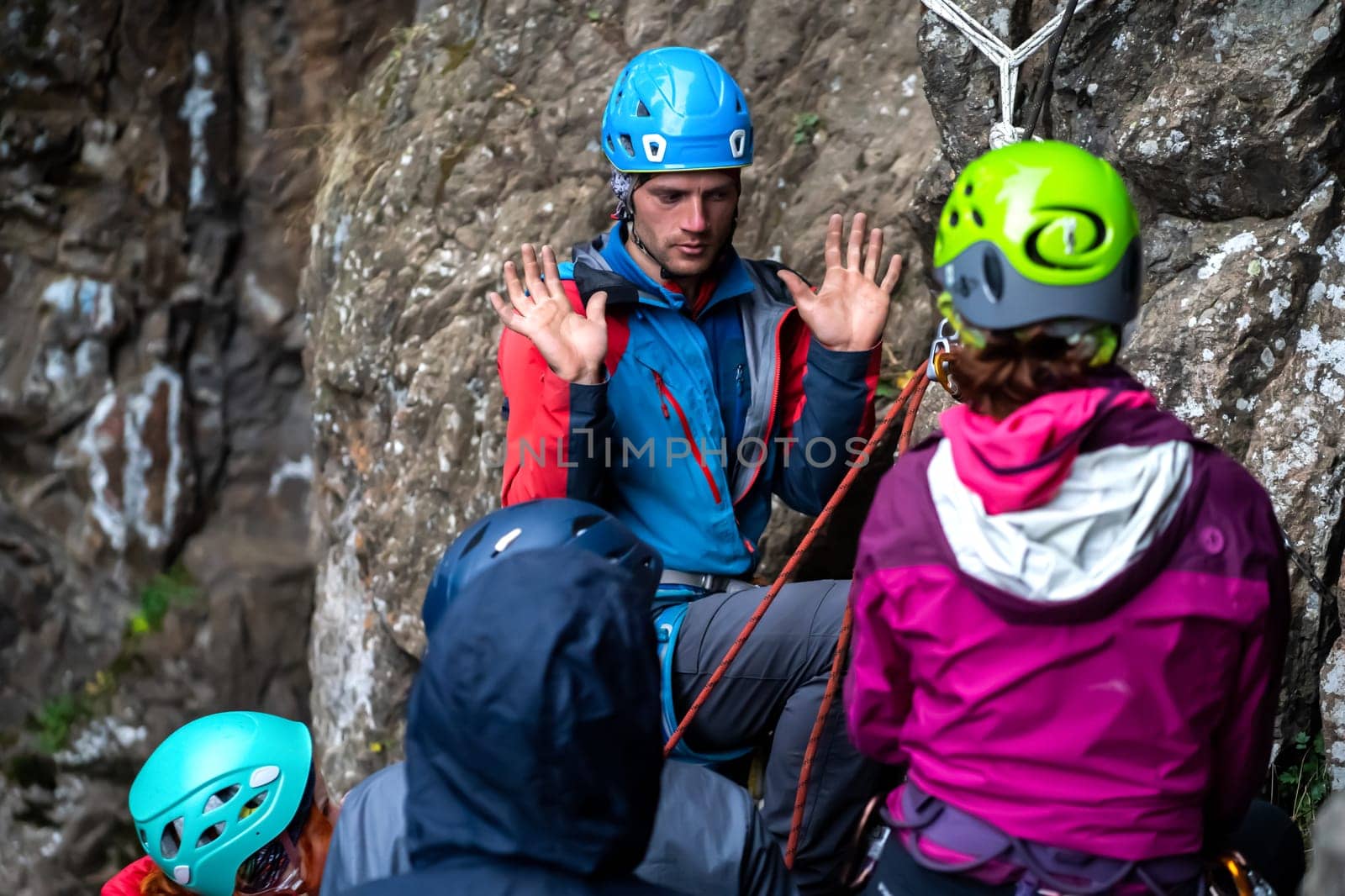 A man, instructor explains to students how to behave in the mountains, a group of people are trained in mountaineering techniques in a camp outdoor on the cliffs.