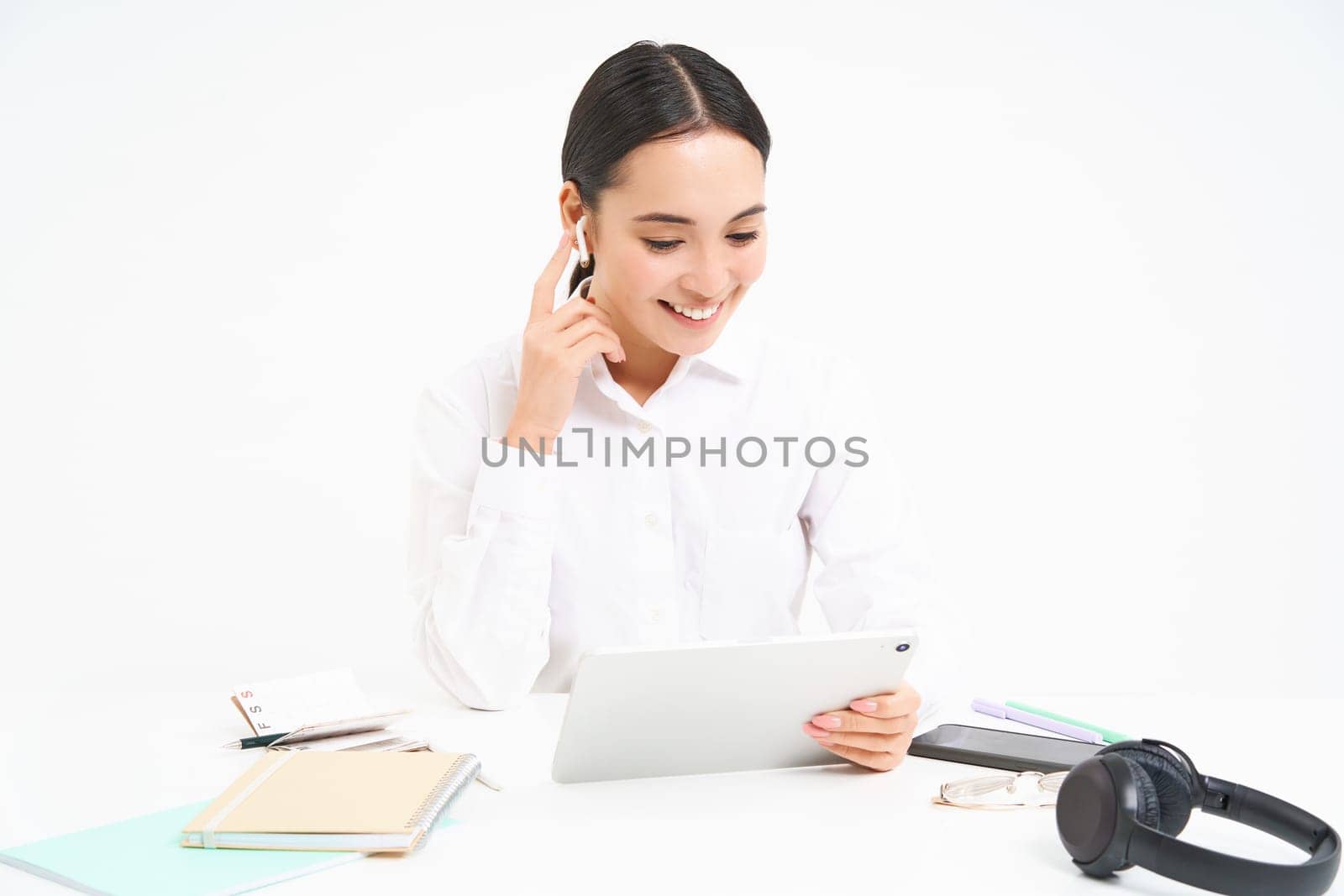 Portrait of korean businesswoman in headphones, connects to meeting on digital tablet, talks on video chat, joins online conference, white background.