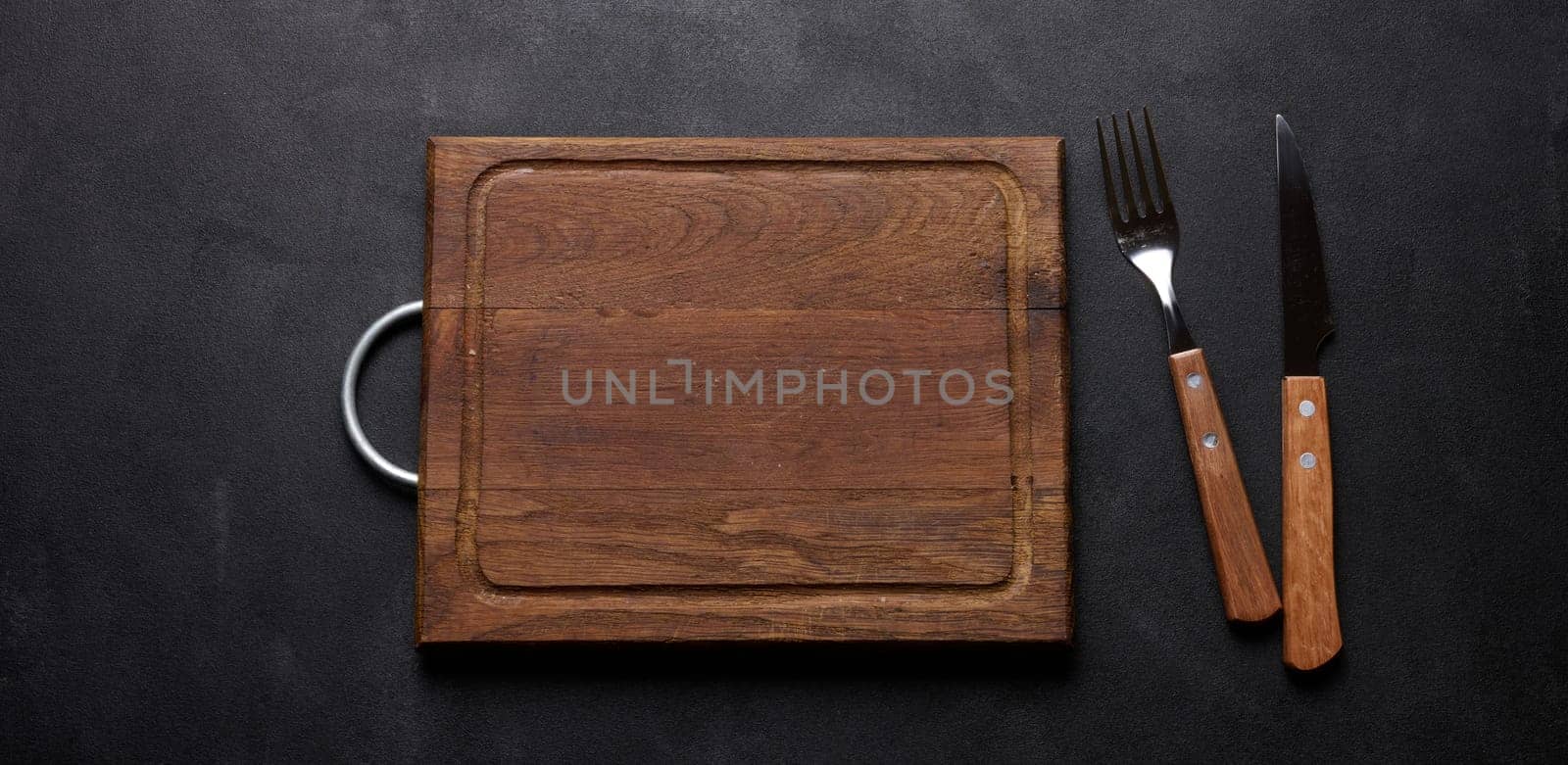 Fork and knife with wooden handle and cutting board on black background, top view by ndanko
