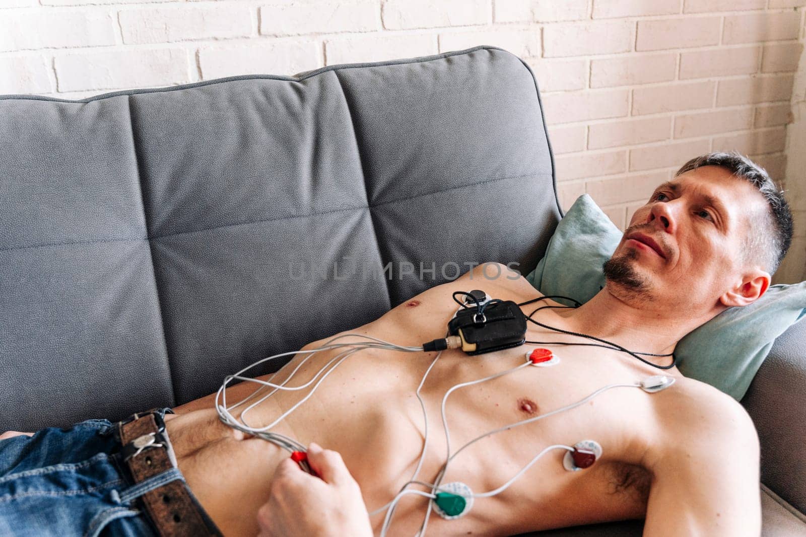 a man lying on a sofa with a Holter heart monitor connected, studying the work of the heart, cardiology. Medical diagnostics. ECG sensors and wires. electrocardiogram, measurement. diagnosis of heart diseases. Health monitoring