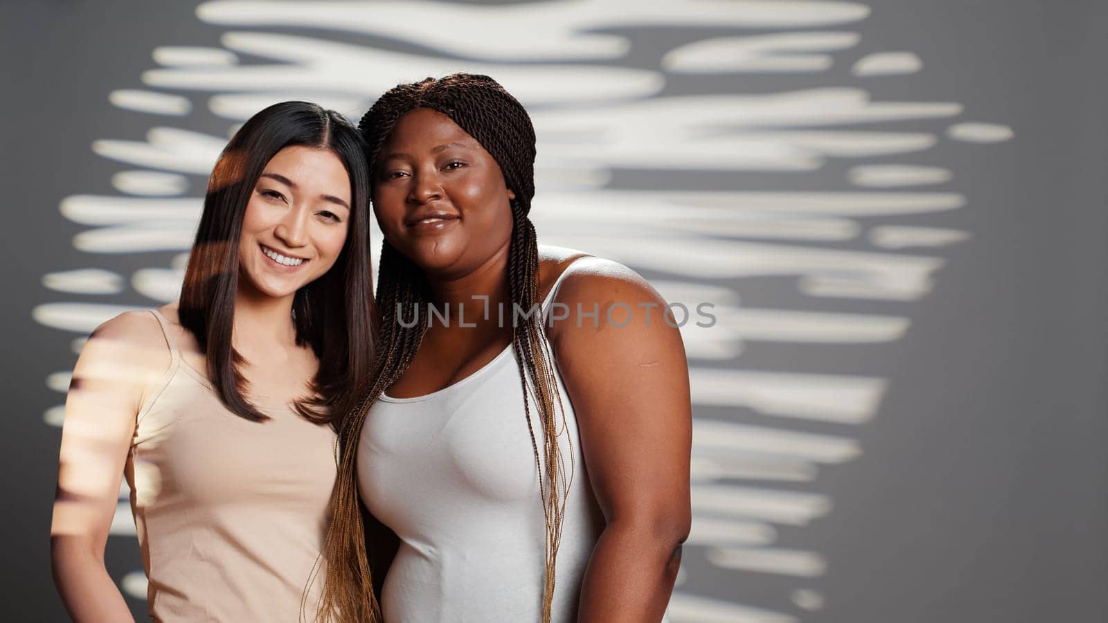 Smiling beauty models hugging and looking at camera, expressing positive emotions and bodycare. Beautiful interracial young women with different body types and skintones posing.