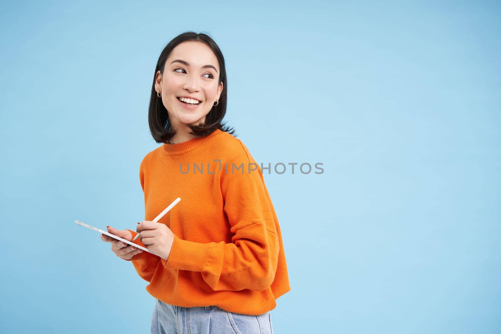 Portrait of young Chinese woman, teacher or student with digital tablet and pencil, writing, taking notes, doing her homework, standing over blue background by Benzoix